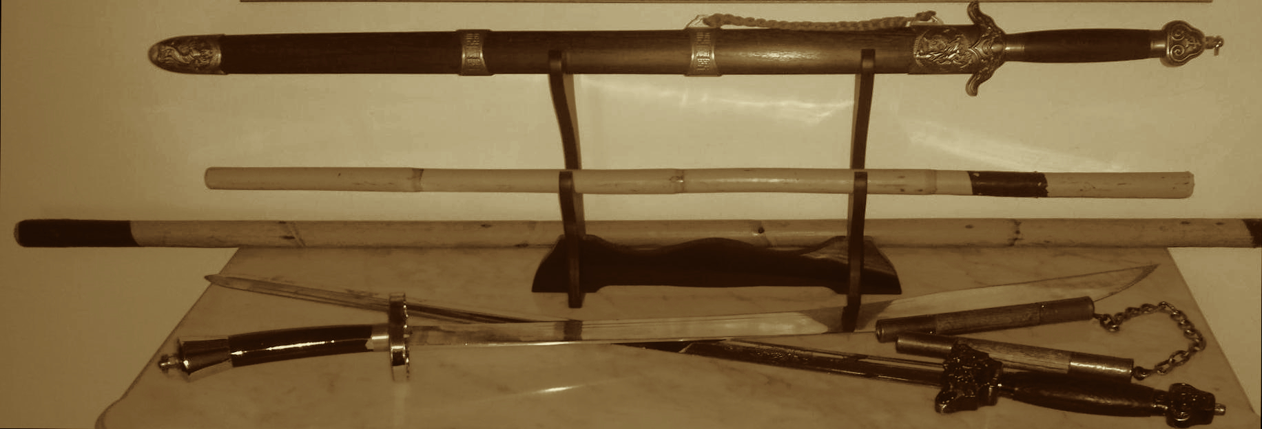Plusieurs armes posées sur une table et un présentoir: épées, sabre, fléau, bâtons