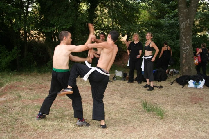 Deux hommes combattant au premier plan, devant plusieurs autres élèves les observant en arrière-plan
